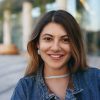 Headshot of attractive latin woman with pretty face looking and smiling cheerfully at camera, posing in urban surroundings on summer day, wearing trendy accessories and denim jacket. City lifestyle